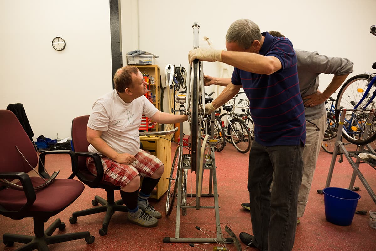 Mehrere Klienten reparieren ein Fahrrad in der Klienten-Fahrradwerkstatt