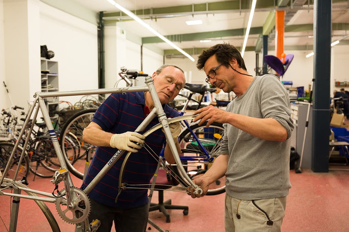 Ein Klient repariert gemeinsam mit einem Betreuer ein Fahrrad in der Fahrradwerkstatt